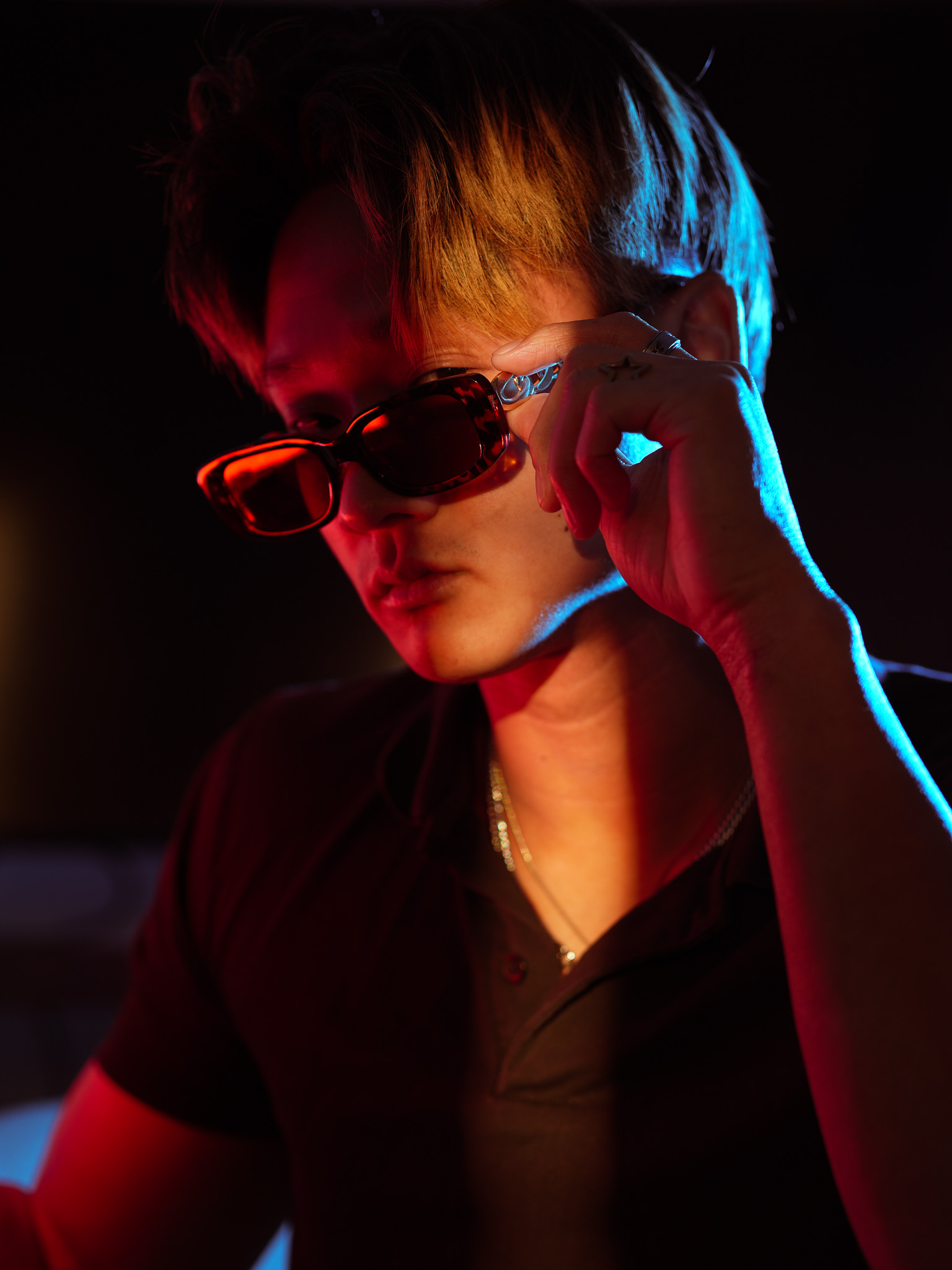 Portrait lit in red and blue, adjusting a pair of tinted sunglasses